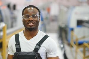 retrato de africano americano masculino ingeniero en uniforme y en pie en industrial fábrica foto