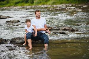 A father teaching his son how to fish on a river outside in summer sunshine. father's day. photo