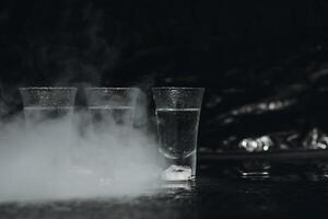 Vodka shots with ice on black table, copy space. photo