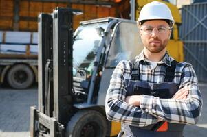 forklift driver in protective vest and forklift standing at warehouse of freight forwarding company, smiling photo