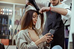 Beautiful woman with long hair using smart phone at beauty salon photo