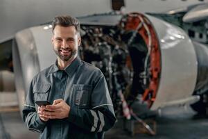 alegre aerolínea mecánico utilizando móvil teléfono en hangar foto