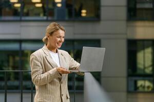 Charming smiling business woman working laptop while standing on modern office terrace photo
