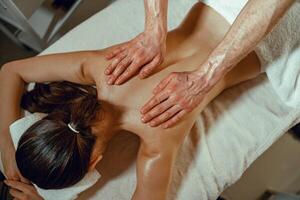 parte superior ver masajista hombre haciendo espalda masaje utilizando petróleo a un mujer en spa salón foto
