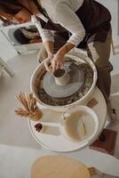 Female potter in apron making shape of clay vase on spinning pottery tool in ceramic workshop photo