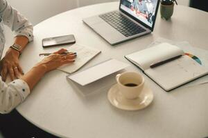 Close up of unrecognisable businesswoman making notes during online conference with colleague photo