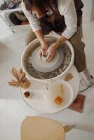 Female potter in apron making shape of clay vase on spinning pottery tool in ceramic workshop photo