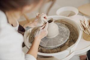 Female potter in apron making shape of clay vase on spinning pottery tool in ceramic workshop photo