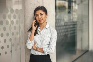 Smiling female freelancer talking phone with client while standing in coworking and looking camera photo