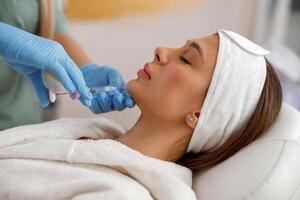 Side view of young woman getting hyaluronic acid injections in chin at beauty salon photo