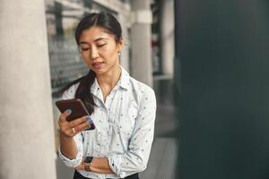 joven bonito negocio mujer mirando en teléfono inteligente mientras en pie en moderno oficina antecedentes foto