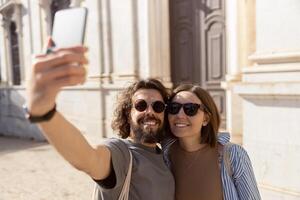 Smiling tourist couple walking in city street and making selfie on phone photo