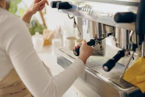 Close up of female barista making coffee in a coffee machine while working in cafe photo