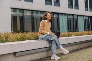 Smiling female manager working on laptop and making notes sitting on background of office building photo