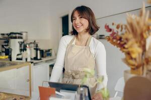 hermosa hembra barista es mirando lejos y sonriente mientras en pie cerca bar mostrador en café foto