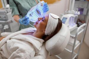 mujer consiguiendo cosmético procedimiento con LED facial mascarilla. fotón terapia foto