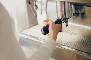 Close up of female barista making coffee in a coffee machine while working in cafe photo