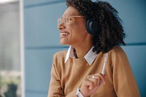 Smiling female manager in headphones listen music and looks away while sitting in office photo