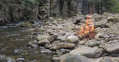 The fire burns on the bank of a mountain stream. Beautiful nature. The concept of rest and travel video