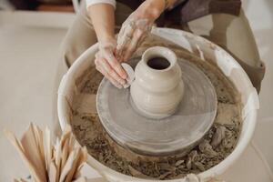 Female potter in apron making shape of clay vase on spinning pottery tool in ceramic workshop photo