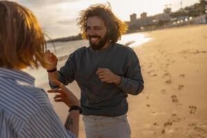 sonriendo Pareja en amor tonto alrededor mientras caminando a lo largo el playa en soleado Ventoso día foto