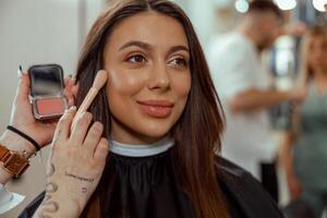 retrato de sonriente mujer consiguiendo maquillaje con un cepillo en belleza salón foto