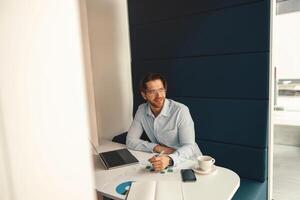 Handsome businessman working on project while using laptop and making notes while sittting in office photo