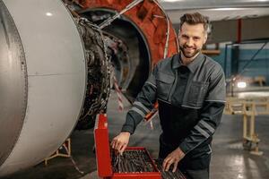 alegre hombre aeronave mecánico utilizando herramienta caja en hangar foto