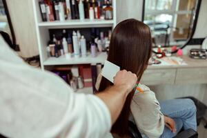 Hairstylist brushing long and shiny brown hair of young woman at beauty salon photo