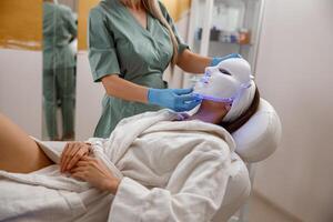 Woman getting cosmetic procedure with LED facial mask. Photon therapy photo