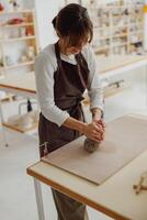 Pretty woman preparing clay to create a mug on a wooden table in pottery studio photo