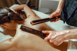 de cerca masculino manos haciendo espalda masaje a mujer utilizando hueco bambú bastones foto