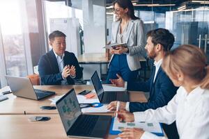 Beautiful business people are using gadgets, talking and smiling during the conference in office photo