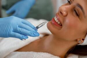 Smiling young woman getting hyaluronic acid injections in lips at beauty salon photo