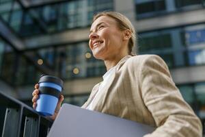 Close up of business woman with laptop going to work with coffee on office building background photo