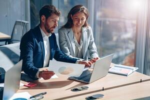 Two smiling business people in modern office explaining statistics data to each other photo