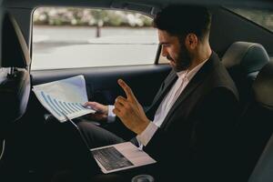 Confidence businessman sitting on car backseat and working with documents and use laptop photo