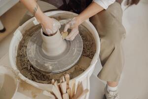 Female potter in apron making shape of clay vase on spinning pottery tool in ceramic workshop photo