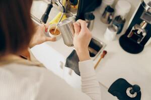 Back view of female barista makes coffee and pours it into a mug while working in coffee shop photo