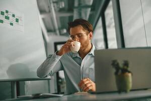 Busy businessman drinking coffee during working on laptop in modern office photo