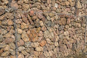 estructura de ingeniería hecha de piedras detrás de una malla metálica para fortalecer la orilla del río cerca del puente de la carretera foto