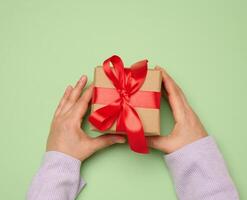 Woman's hand holding a gift box wrapped in a red silk ribbon on a green background photo