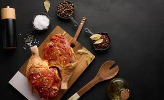 Raw chicken drumsticks seasoned on a wooden board, accompanied by salt and peppercorns, viewed from the top photo