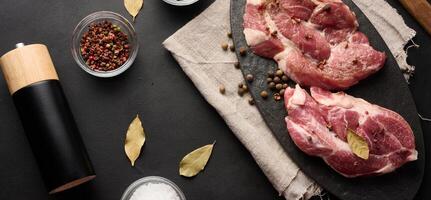 Two raw pork neck steaks on a board and spices for cooking. Top view photo