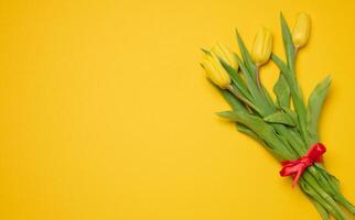 Bouquet of blooming tulips with green leaves on a yellow background, top view photo