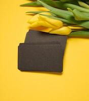 Blank paper black business card and a bouquet of yellow tulips on a yellow background photo