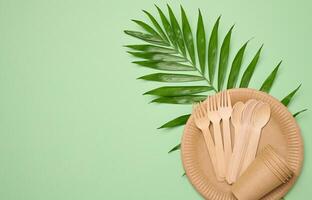 Paper plates and cups, wooden spoons and forks on a green background photo