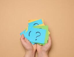 Female hands hold paper sheets with a drawn question mark on a beige background, photo