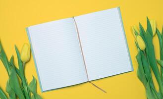 Open notebook with white blank sheets and a bouquet of yellow tulips on a yellow background photo