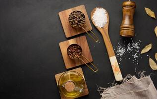 Salt, allspice, peppercorns and olive oil in a bottle on a black table, top view photo